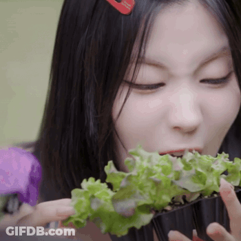 A Woman With A Red Hair Clip Is Eating Lettuce From A Container GIF