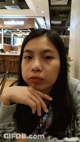 A Woman With A Ring On Her Finger Is Sitting In Front Of A Sandwich Shop GIF