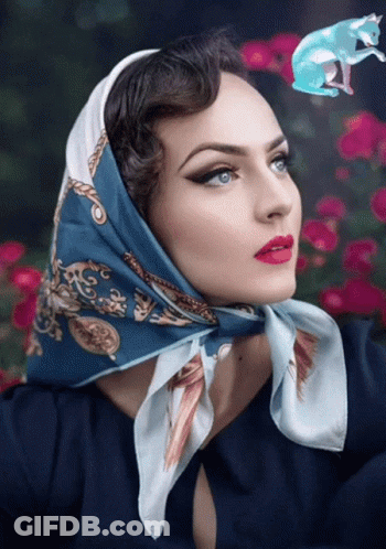 A Woman With A Scarf Around Her Head Has A Blue Cat Flying Above Her Head GIF