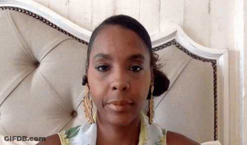 A Woman With A Scarf Around Her Neck Is Sitting In Front Of A Bed GIF