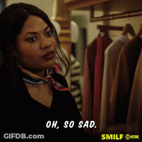 A Woman With A Scarf Around Her Neck Is Standing In Front Of A Closet And Says Oh So Sad GIF