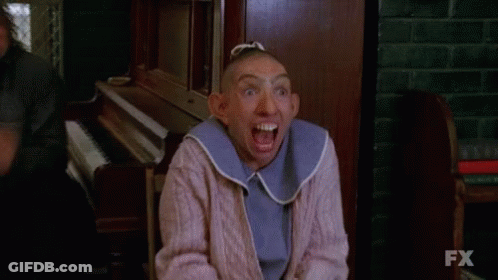 A Woman With A Shaved Head And A Bib On Her Neck Is Making A Funny Face . GIF