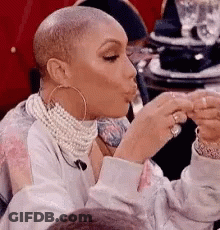 A Woman With A Shaved Head Is Sitting At A Table Eating A Sandwich . GIF