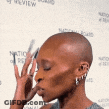 A Woman With A Shaved Head Is Standing In Front Of A National Board Of Review Banner GIF