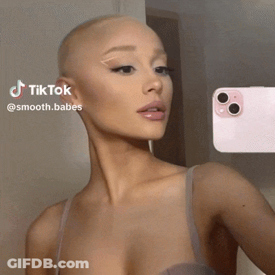 A Woman With A Shaved Head Is Taking A Selfie In Front Of A Pink Phone . GIF