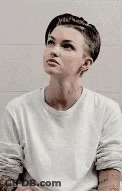 A Woman With A Shaved Head Is Wearing A White Shirt . GIF