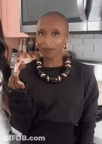 A Woman With A Shaved Head Wearing A Black Sweater And A Black Necklace GIF