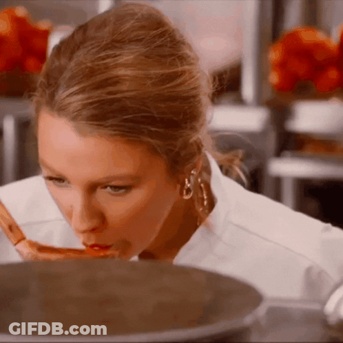 A Woman With A Spoon In Her Mouth Looks At Something In A Pot GIF