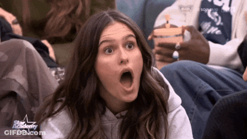 Surprised Woman Sitting In Front Of Star Academy Sign GIF