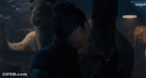 A Woman With A Surprised Look On Her Face Is Standing In A Dark Room With A Statue In The Background GIF