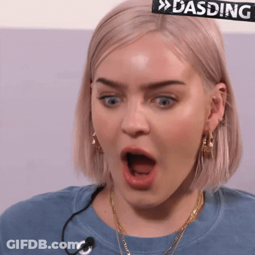 A Woman With A Surprised Look On Her Face Is Wearing A Blue Shirt With A Microphone . GIF