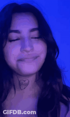 A Woman With A Tattoo Of A Heart On Her Neck Is Smiling With Her Eyes Closed . GIF