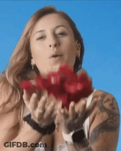 A Woman With A Tattoo On Her Arm Is Blowing Red Roses Into The Air GIF