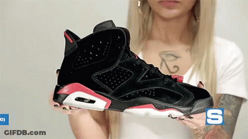 A Woman With A Tattoo On Her Chest Is Holding A Pair Of Black And Red Sneakers .. GIF