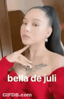 A Woman With A Tattoo On Her Chest Is Wearing A Red Dress And Holding Her Hand To Her Chin . GIF