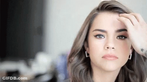A Woman With A Tattoo On Her Wrist Is Touching Her Hair And Looking At The Camera . GIF
