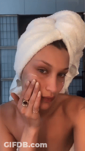 A Woman With A Towel Wrapped Around Her Head Is Applying A Cream To Her Face GIF
