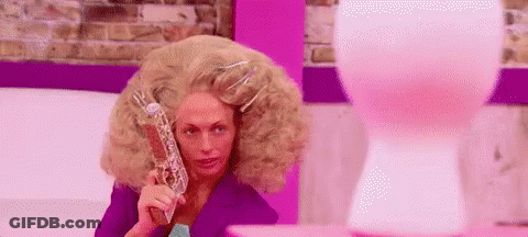 A Woman With A Very Large Wig Is Holding A Gun In Front Of A Pink Balloon . GIF