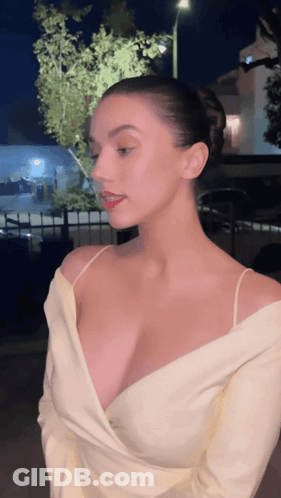 A Woman With A Very Plunging Neckline Is Standing In Front Of A Building At Night GIF