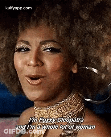 A Woman With An Afro Is Wearing A Gold Necklace And Earrings And Is Talking . GIF