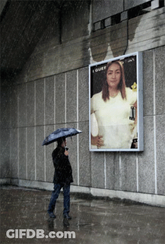 A Woman With An Umbrella Stands In Front Of A Billboard That Says I Guess GIF
