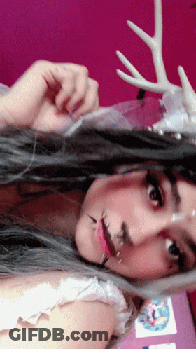 A Woman With Antlers On Her Head Is Wearing A White Top GIF