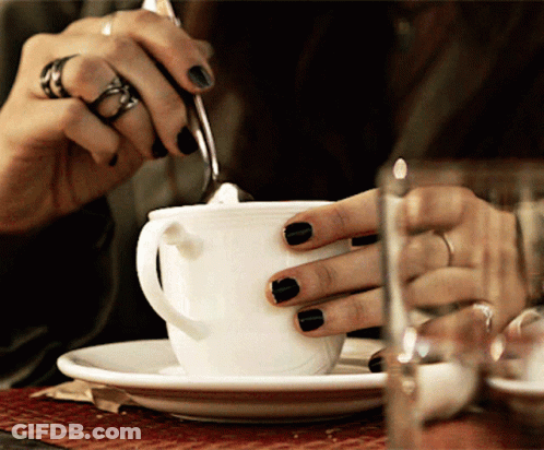 A Woman With Black Nail Polish Is Stirring A Cup Of Coffee GIF