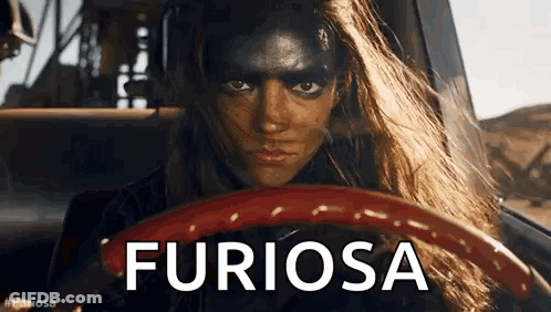 A Woman With Black Paint On Her Face Is Driving A Car And The Word Furiosa Is On The Steering Wheel . GIF