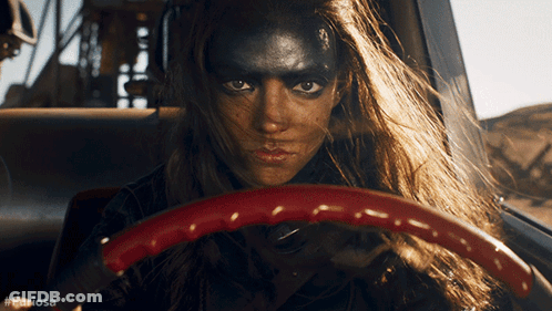 A Woman With Black Paint On Her Face Is Driving A Car With The Hashtag #Furiousa GIF