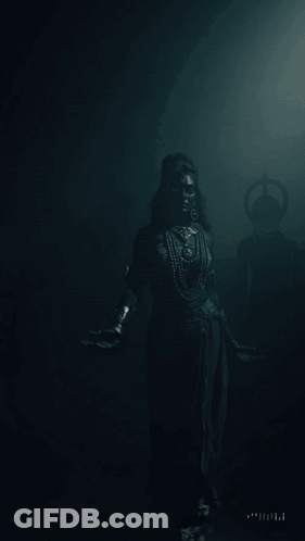 A Woman With Black Paint On Her Face Is Standing In A Dark Room With Her Arms Outstretched GIF