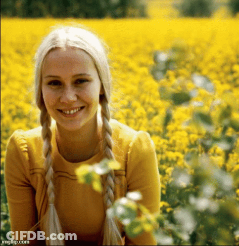 A Woman With Blonde Braids Is Smiling In A Field Of Yellow Flowers .. GIF