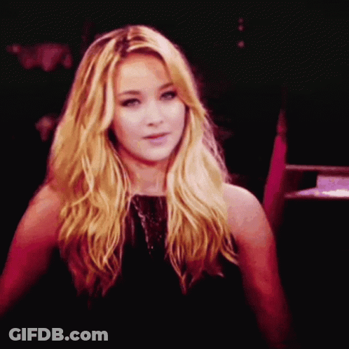 A Woman With Blonde Hair And A Black Dress Looks At The Camera GIF
