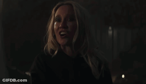 A Woman With Blonde Hair And A Black Shirt Smiles In The Dark GIF