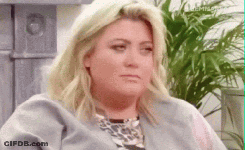 A Woman With Blonde Hair And A Leopard Print Shirt Is Sitting In Front Of A Plant . GIF