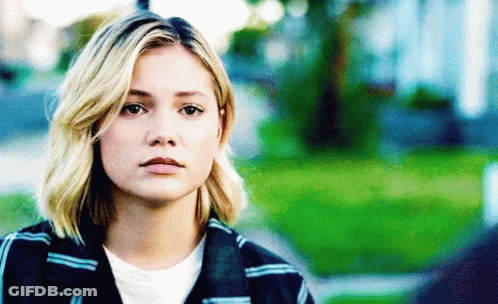 A Woman With Blonde Hair And A Plaid Jacket Is Looking At The Camera GIF