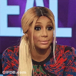 A Woman With Blonde Hair And A Ponytail Is Making A Funny Face While Sitting In Front Of A Sign That Says Call GIF
