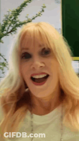 A Woman With Blonde Hair And A White Shirt Is Smiling GIF