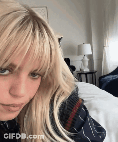 A Woman With Blonde Hair And Bangs Is Laying On A Bed GIF
