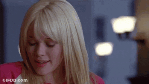 A Woman With Blonde Hair And Bangs Is Smiling While Wearing A Pink Shirt . GIF