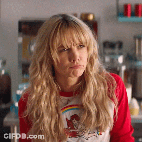 A Woman With Blonde Hair And Bangs Is Wearing A Red Shirt And Making A Face . GIF