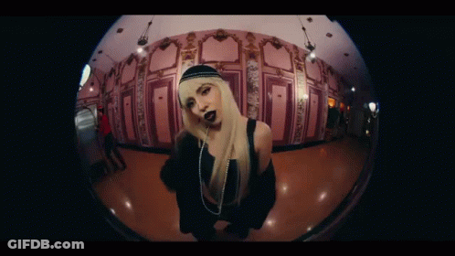 A Woman With Blonde Hair And Black Lipstick Is Standing In A Hallway . GIF