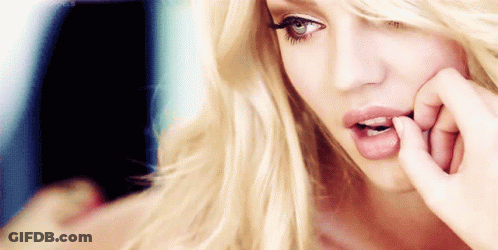 A Woman With Blonde Hair And Blue Eyes Is Biting Her Nails GIF