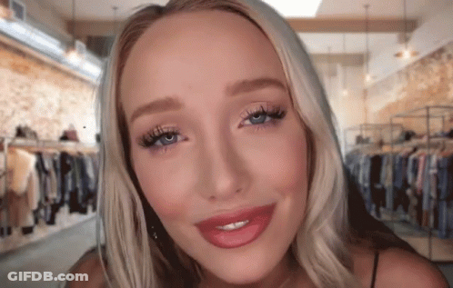 A Woman With Blonde Hair And Blue Eyes Is Smiling In Front Of A Clothing Store GIF