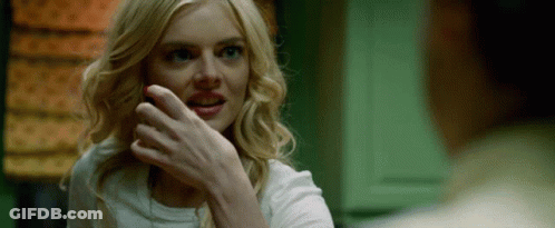 A Woman With Blonde Hair And Blue Eyes Is Smiling While A Man Holds Her Hand To Her Face . GIF