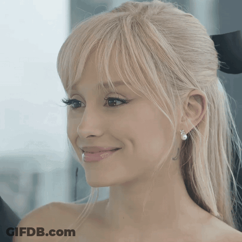 A Woman With Blonde Hair And Pearl Earrings Smiles For The Camera GIF