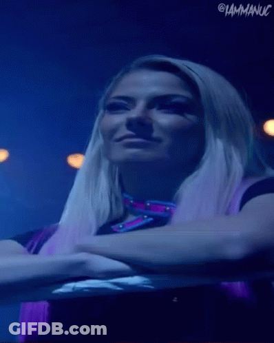 A Woman With Blonde Hair And Purple Hair Is Standing In A Dark Room With Her Arms Crossed . GIF