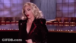 A Woman With Blonde Hair And Red Lips Is Standing On A Stage In A Black Jacket . GIF