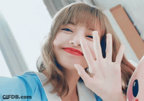 A Woman With Blonde Hair And Red Lips Is Waving Her Hand At The Camera . GIF