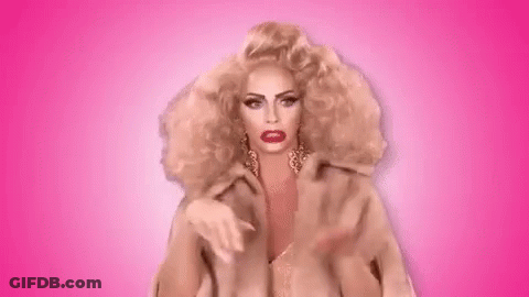 A Woman With Blonde Hair And Red Lipstick Is Making A Peace Sign With Her Hands On A Pink Background . GIF