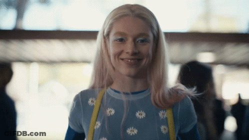 A Woman With Blonde Hair And White Eye Shadow Smiles For The Camera GIF